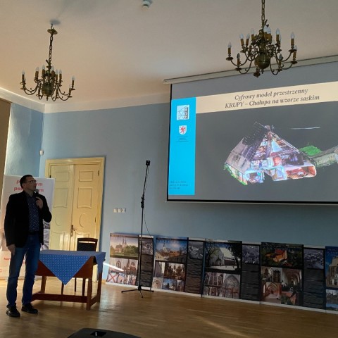 Powiększ obraz: Kustosz Krzysztof tymbarski omawia zagadnienia cyfryzacji pokazując slajd z cyfrowym modelem chałupy w Krupach.